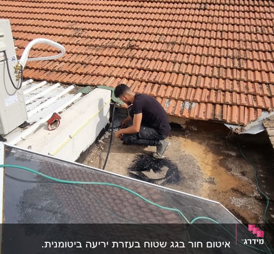 אדם עובד על איטום גג עם חומר שחור